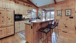 A wooden cabin-style kitchen with a central island, bar stools, and a large window.