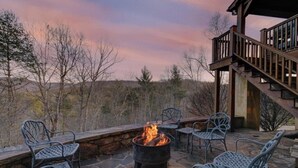 An outdoor patio with a fire pit, stone flooring, and metal chairs.