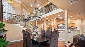 A spacious dining area with a dark wooden table and patterned chairs, a chandelier, and a staircase with ornate railings. - 5 Bdr Beautiful Riverfront Home with Dock! (Bullhead City)