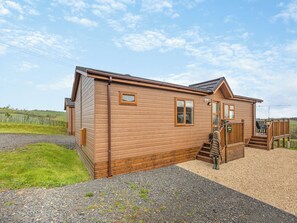 A wooden cabin with a porch, a staircase, and a gravel driveway.