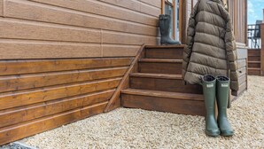 Un bâtiment en bois avec un escalier menant à une porte, une personne portant un long manteau et des bottes, et un ciel dégagé.