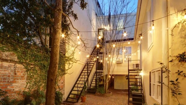 A courtyard with brick flooring, a staircase, and string lights. - Jones St Jewel, Charming | Central | Pet-Friendly! (Savannah)