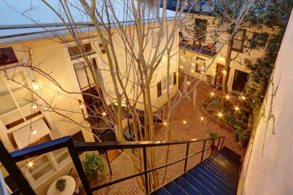 Une cour intérieure avec un escalier, des arbres et des guirlandes lumineuses.