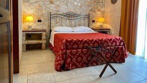 Une chambre avec un mur en pierre, un lit recouvert d’une courtepointe rouge, deux lampes de chevet et une table de nuit en bois.