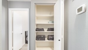 Ein begehbarer Kleiderschrank mit mehreren Regalen und Ablageflächen, ausgestattet mit ordentlich gefalteten Handtüchern und einigen Kleidungsstücken.