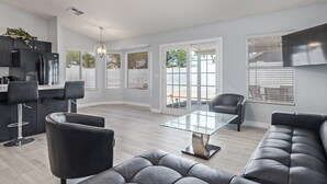 Ein modernes Wohnzimmer mit einem Glastisch, Ledersofas und einer Küchenzeile mit schwarzen Schränken und Geräten.