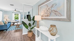 Een woonkamer met een blauwe bank, een ronde stoel, een potplant, een lamp en een kunstwerk van een zeeschildpad.