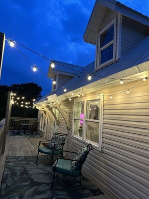 A covered outdoor area with string lights, a wooden deck, and two chairs. - 3bd 2ba Sleeps 10 Golf Cart Included Pet Friendly (Panama City Beach)