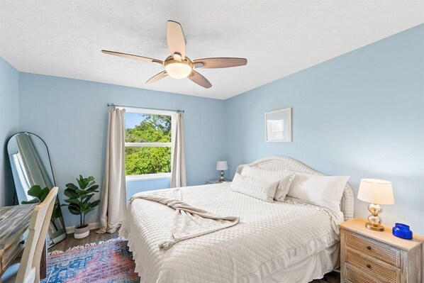 A bedroom with a bed, a ceiling fan, a window with curtains, a bedside table with a lamp, and a plant. - 3bd 2ba Sleeps 10 Golf Cart Included Pet Friendly (Panama City Beach)