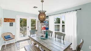 A dining area with a wooden table, chairs, a hanging light fixture, and a view through a glass door. - 3bd 2ba Sleeps 10 Golf Cart Included Pet Friendly (Panama City Beach)