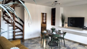 Un salon avec un escalier en colimaçon, une table à manger dressée avec de la vaisselle, un canapé et un téléviseur posé sur un meuble.
