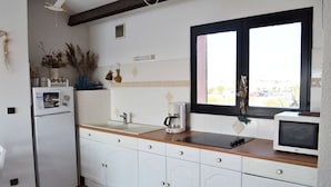 Eine Küche mit weißen Schränken, einer Holzausziehtafel, einem Kühlschrank, einer Kaffeemaschine und einer Mikrowelle.