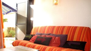 A room with a striped orange sofa, a small table, and a window with blinds. - 2-room apartment sleeps 4 PORT LEUCATE NATURISME (PORT LEUCATE NATURISME)