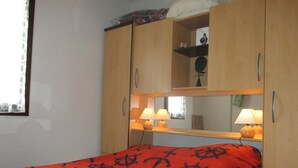 A bedroom with a bed, two bedside lamps, a wooden wardrobe, and a mirror. - 2-room apartment sleeps 4 PORT LEUCATE NATURISME (PORT LEUCATE NATURISME)