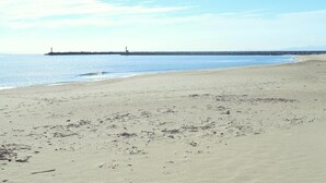 Een breed zandstrand met een rustige zee en een pier in de verte.