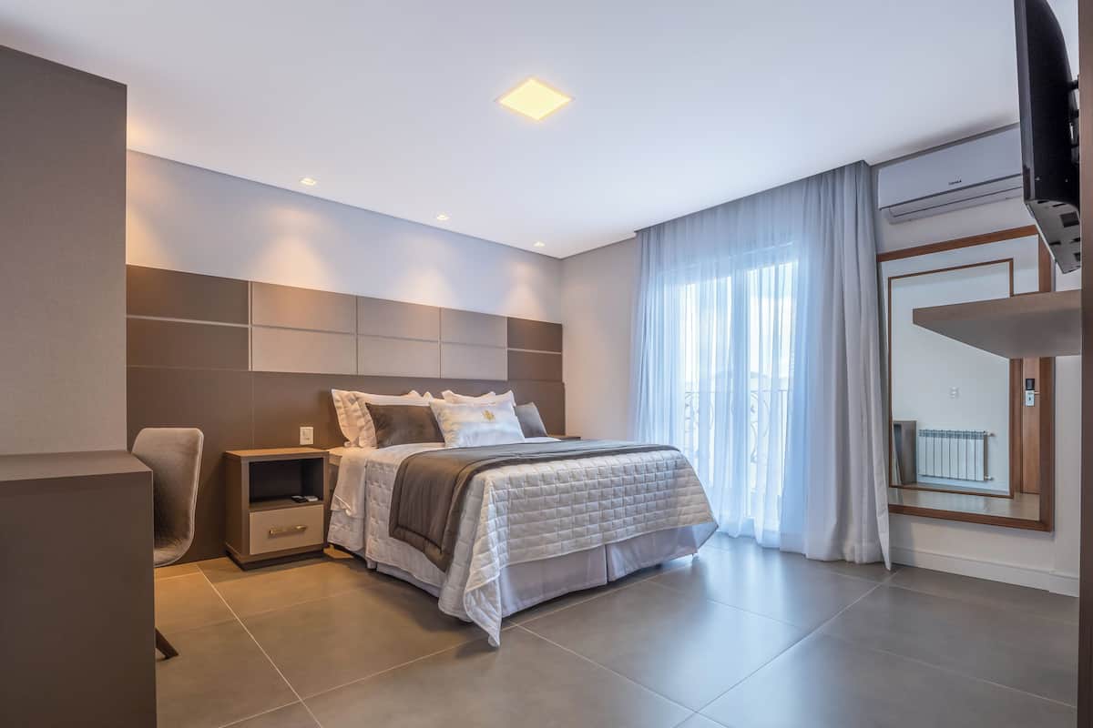 A modern bedroom with a large bed, bedside tables, a chair, and a view of the outdoors through a window with curtains.