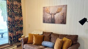 Een knus woongedeelte met een bruine bank, een houten salontafel en een schilderij van een eland aan de muur.