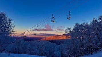 A ski lift with chairs suspended from cables, surrounded by snow-covered trees and a mountainous backdrop.