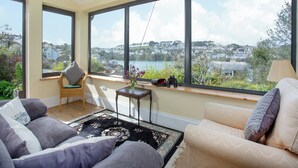 Ein geräumiges Wohnzimmer mit großen Fenstern und Blick auf eine Küstenstadt.