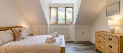 A bedroom with a sloped ceiling, a bed with pillows, a dresser, and a window with blinds.