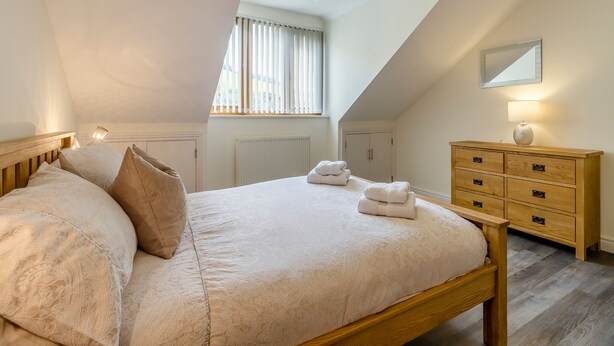 A bedroom with a sloped ceiling, a bed with a wooden headboard, a dresser with drawers, and a mirror on the wall. - 5 bedroom accommodation in llanafan/Aberystwyth (llanafan/Aberystwyth)