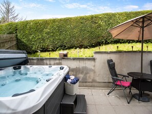 A hot tub with a wooden bench and a chair, a table with a chair, and a patio umbrella. - 5 bedroom accommodation in llanafan/Aberystwyth (llanafan/Aberystwyth)