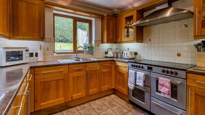 A kitchen with wooden cabinets, a stainless steel range hood, a double oven, a microwave, and a window with a view of greenery. - 5 bedroom accommodation in llanafan/Aberystwyth (llanafan/Aberystwyth)
