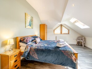 A bedroom with a sloped ceiling, a skylight, a bed with floral bedding, a wooden nightstand, and a chair with a blanket. - 5 bedroom accommodation in llanafan/Aberystwyth (llanafan/Aberystwyth)