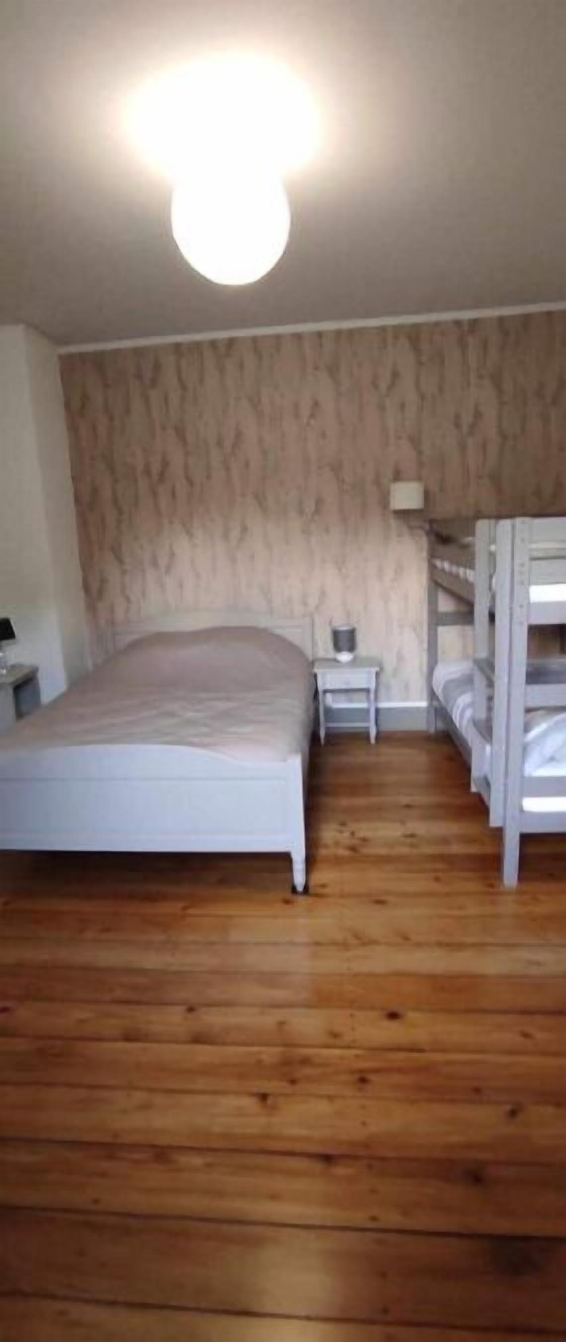 Ein Zimmer mit einem Etagenbett, einem Einzelbett, einem Nachttisch und einer Lampe.