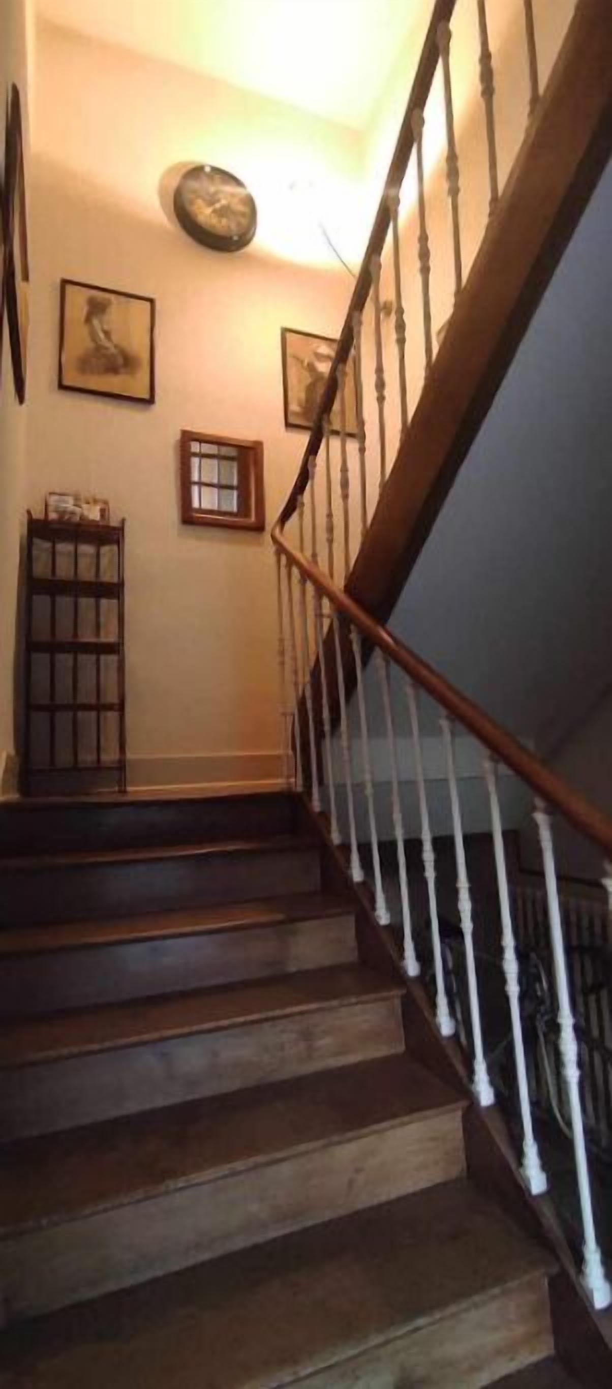 Un escalier en bois, avec des balustrades blanches, menant à un palier.