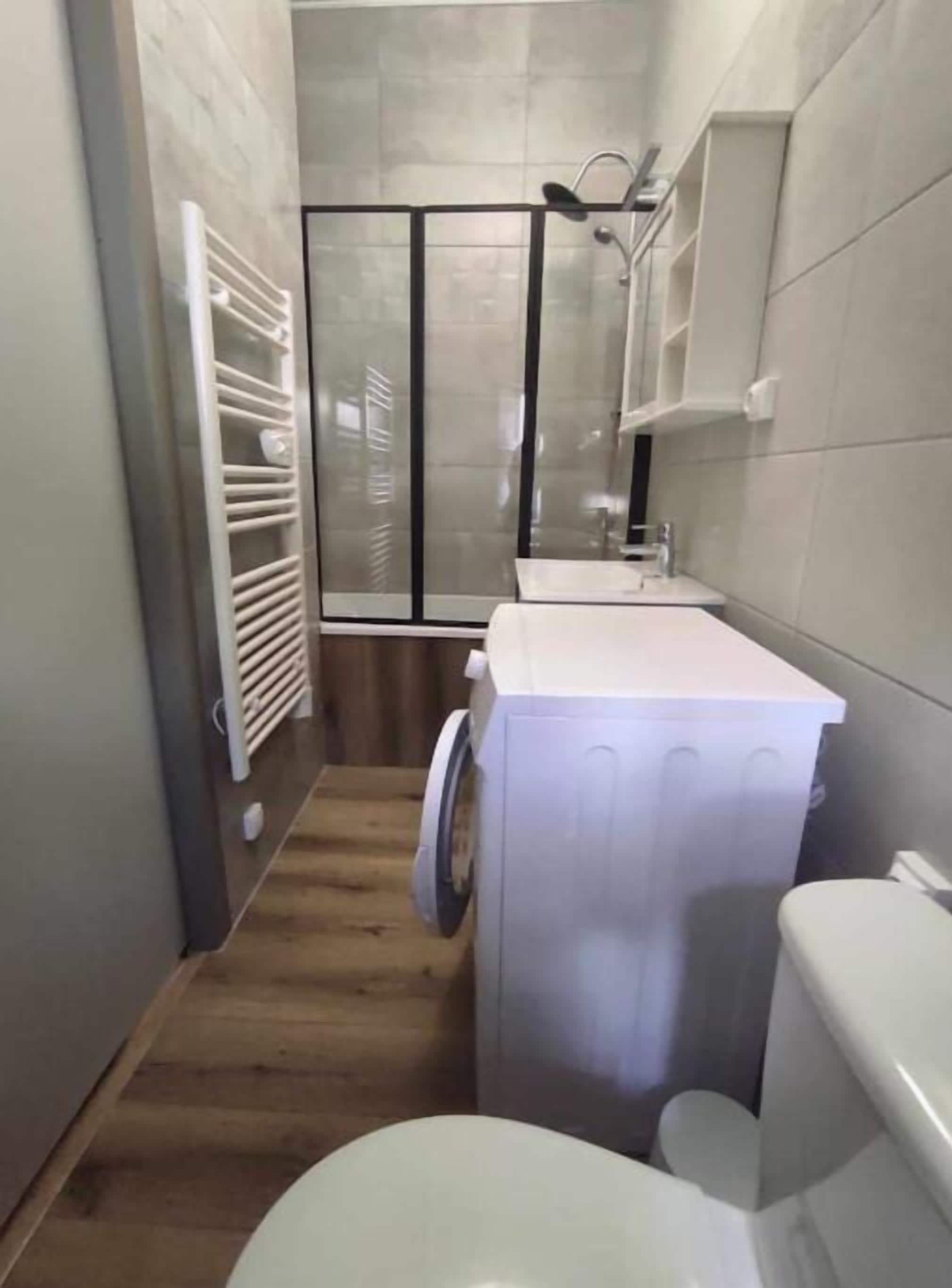 Un baño pequeño con ducha, lavadora e inodoro.