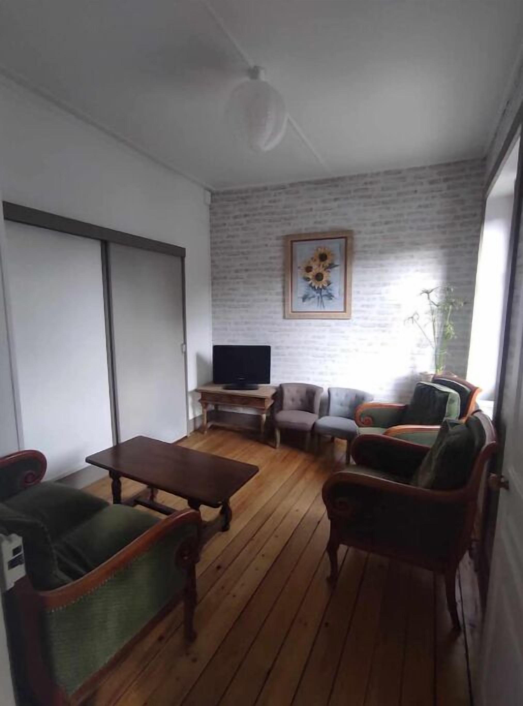 Un salon avec un plancher en bois, un téléviseur posé sur un meuble et un tableau encadré accroché au mur.