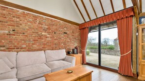 Una habitación con pared de ladrillo, techo de madera, un sofá, una mesa de centro de madera y un gran ventanal con cortinas.