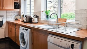 Une cuisine moderne avec des meubles en bois, un lave-vaisselle encastré, un lave-linge et une grande fenêtre donnant sur le jardin.