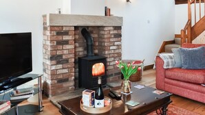 Un salon avec une cheminée en briques, un téléviseur, une table basse avec des livres et une bouteille, et un canapé rouge.