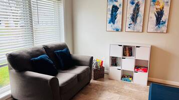 Una sala de estar con un sofá gris, cojines azules, una estantería blanca y tres obras de arte enmarcadas en la pared.