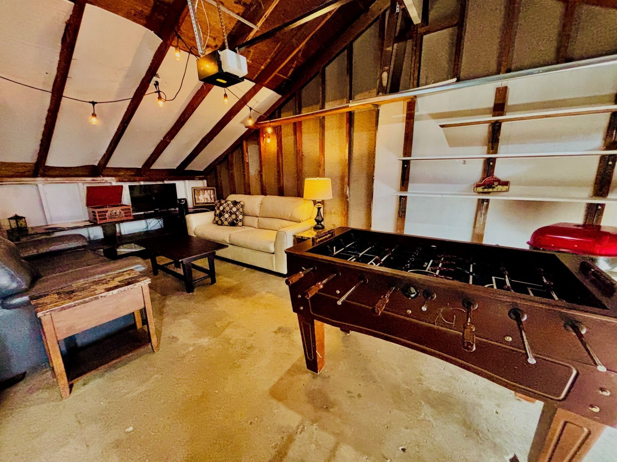 A cozy loft with exposed wooden beams, a sofa, a foosball table, and a TV.
