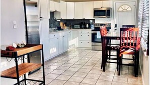 A modern kitchen with white cabinets, a stainless steel refrigerator, a microwave, and a dining area with a wooden table and chairs.
