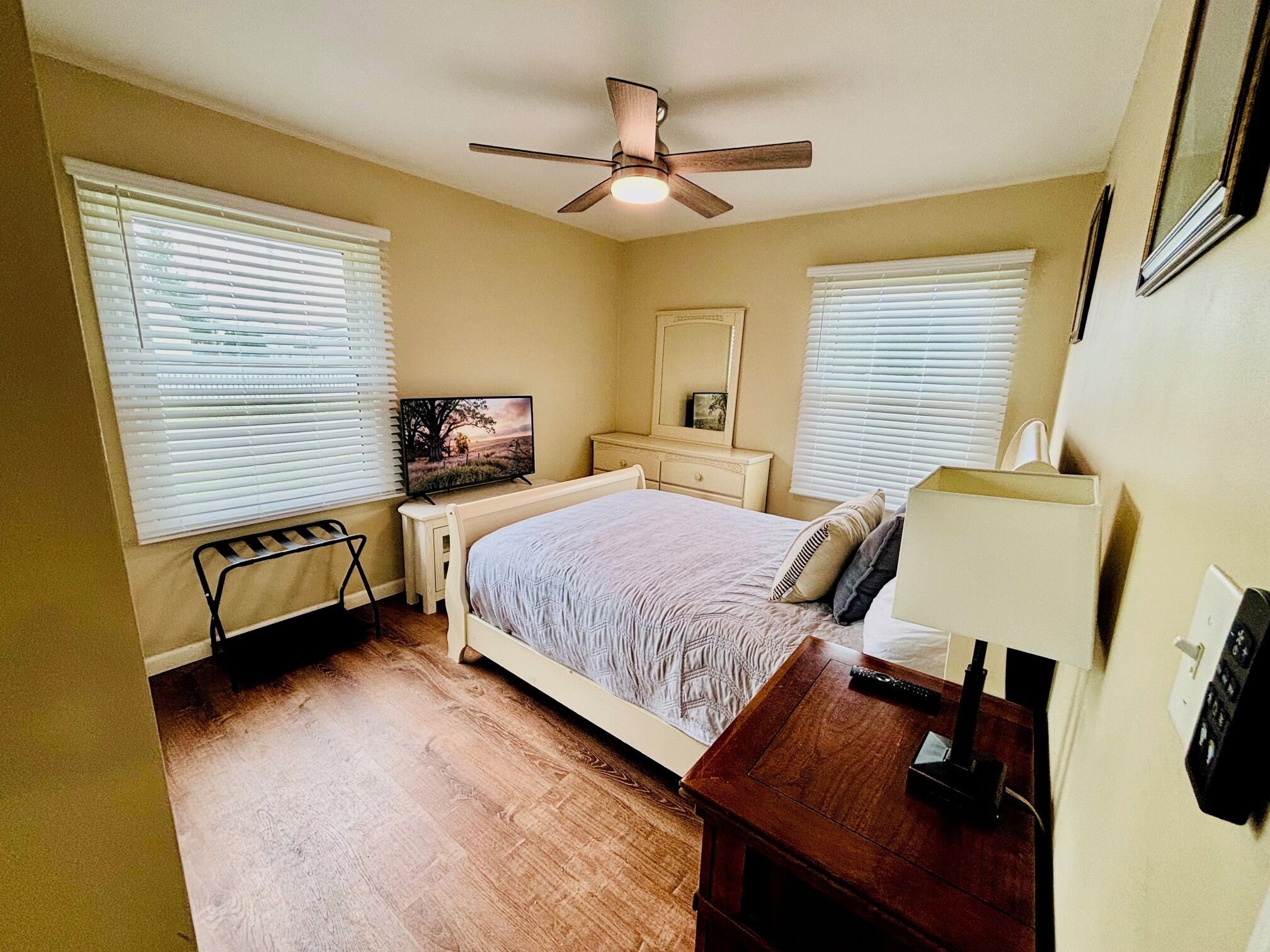 Une chambre à coucher comprenant un lit, une table de chevet, une commode, un ventilateur de plafond et un téléviseur.