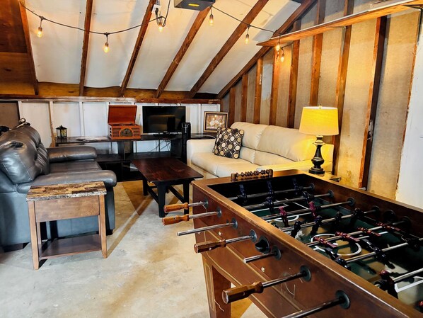 A cozy living room with a sofa, a coffee table, a foosball table, and a television.