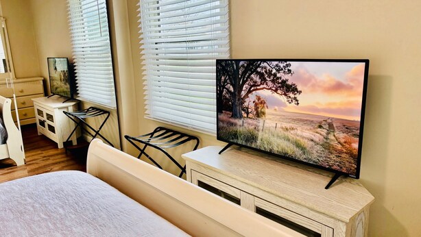 A bedroom with a bed, a desk, a chair, and a TV on a wooden cabinet.