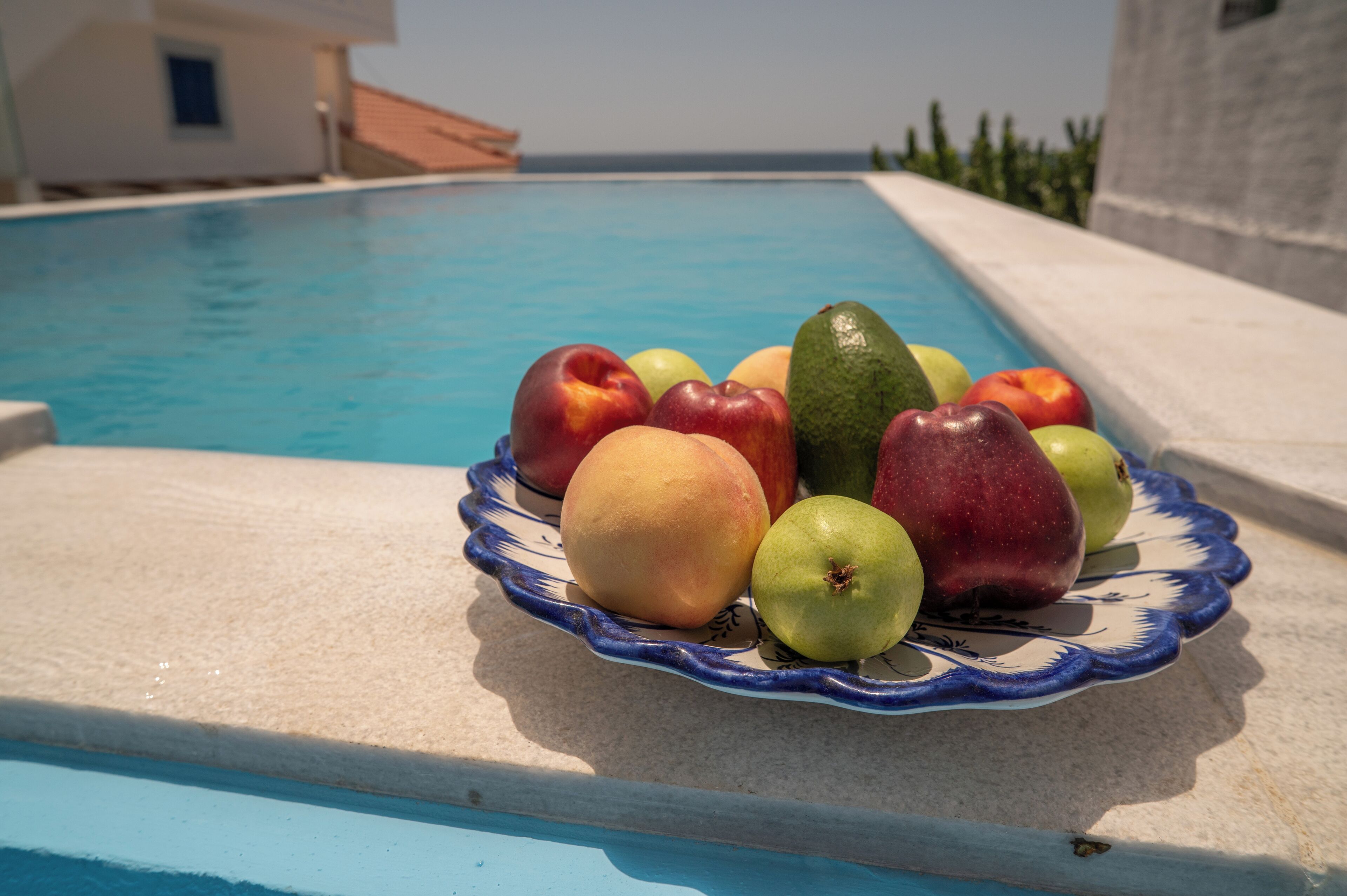Un frutero con diversas frutas sobre una mesa junto a la piscina.