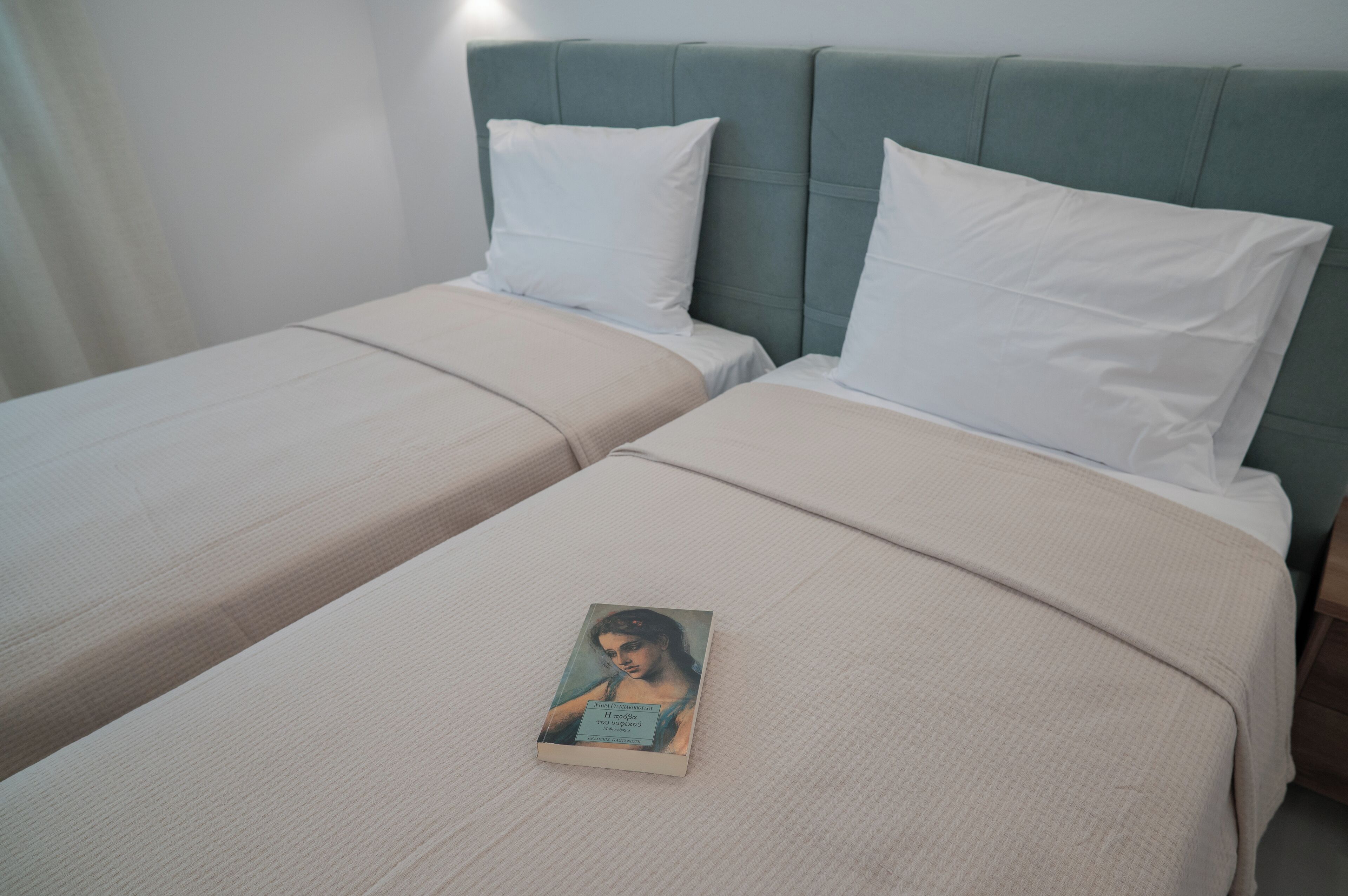 Une chambre d’hôtel avec deux lits simples, chacun agrémenté d’un oreiller blanc et d’une couvre-lit beige. Un livre est posé sur le lit, au premier plan.