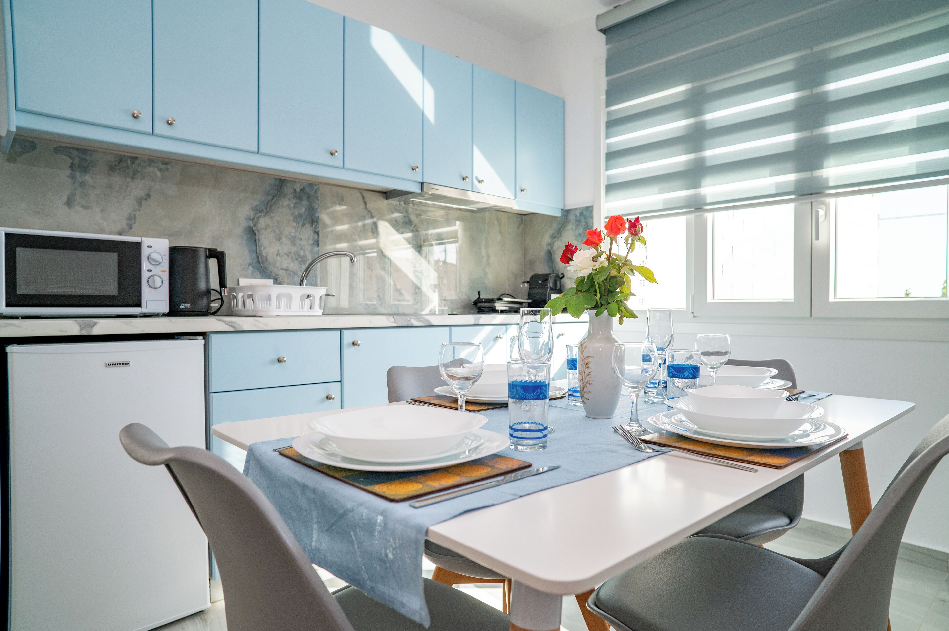 Een moderne keuken met blauwe kastjes, een magnetron en een eettafel gedekt voor vier personen.