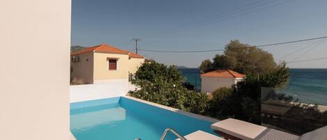 A swimming pool with lounge chairs, a view of the sea, and a building with a red roof.