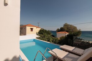 A swimming pool with lounge chairs, a view of the sea, and a building with a red roof. - Kontemare Seascape (Samos)