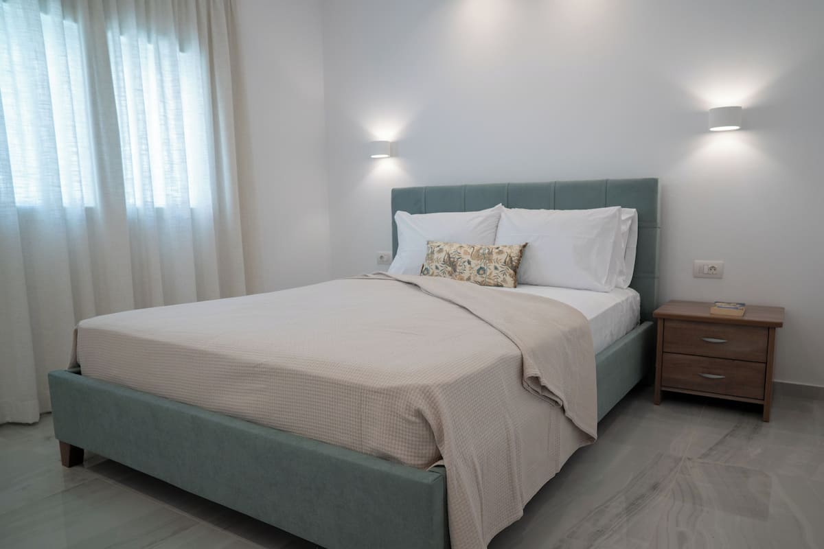 Un dormitorio con cama, mesitas de noche y ventana con cortinas.