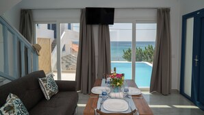 Un comedor con una mesa lista para dos personas, un sofá y vista al mar a través de amplios ventanales.