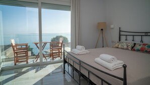 Un dormitorio con un ventanal grande, una cama con dos almohadas, una lámpara de noche y vistas al mar.