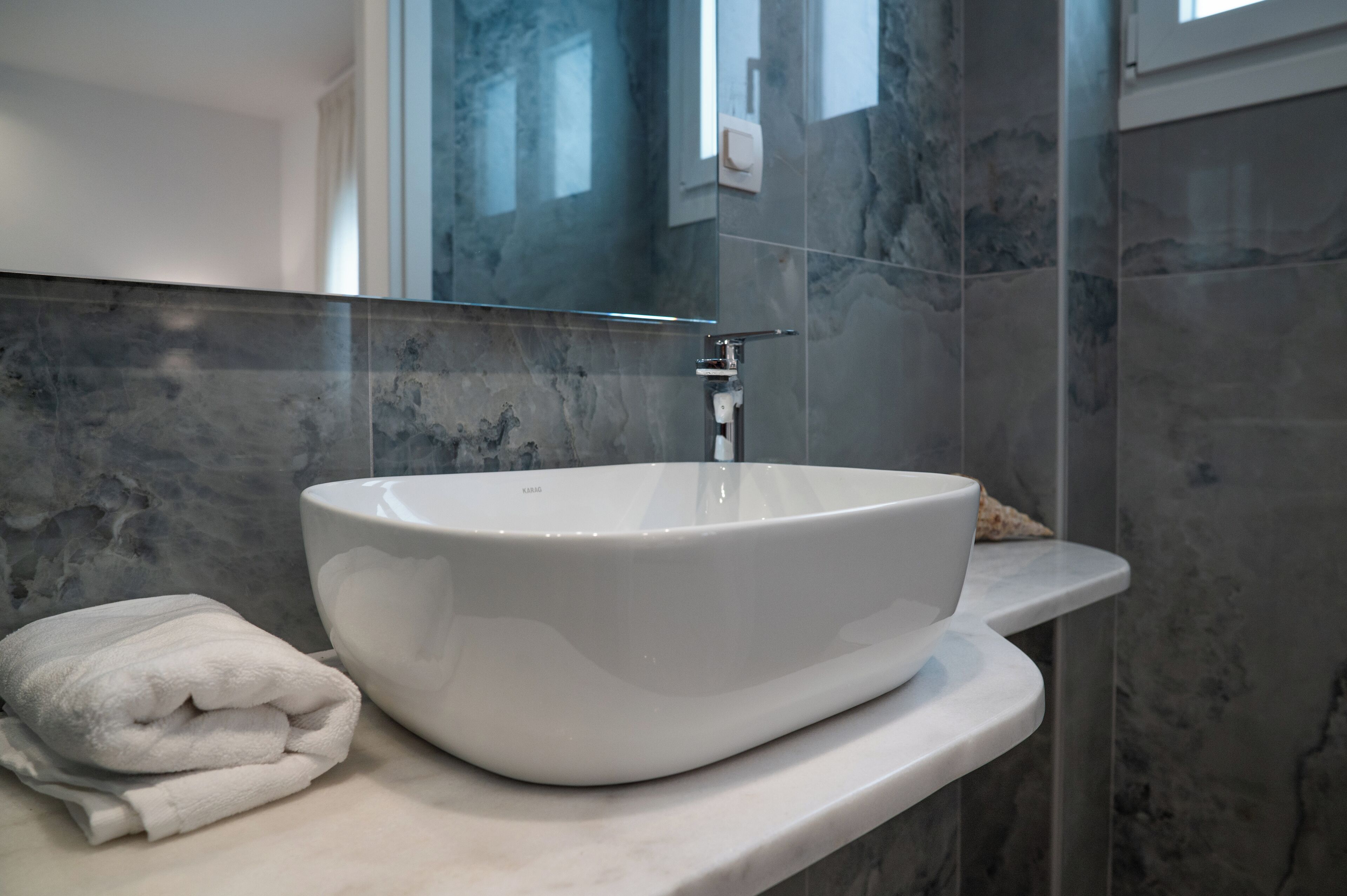 A bathroom with a large white vessel sink, a towel, and marble walls.